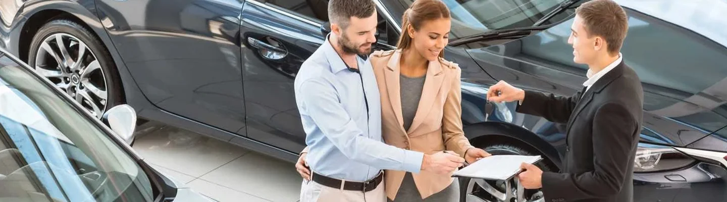 couple speaking with salesperson in showroom discussing Used vs New car purchase
