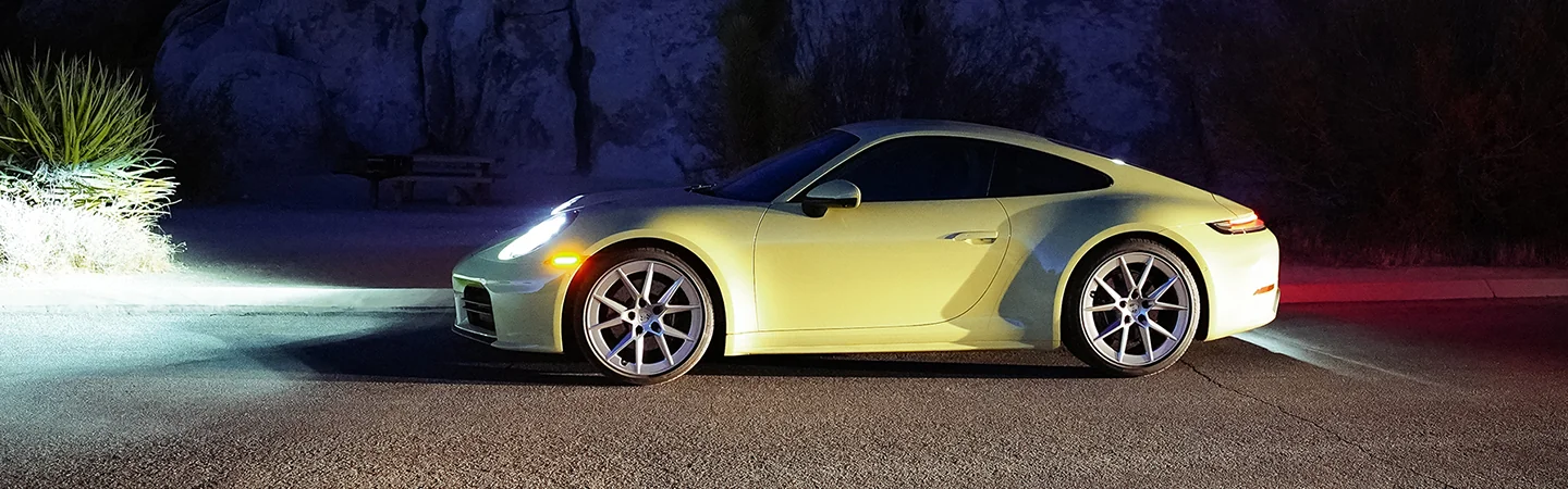 a Yellow 2026 Porsche 911 Carrera driving at night with headlights on