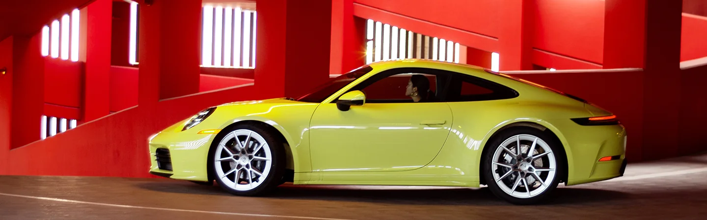 a bright yellow 2026 Porsche 911 Carrera ina bright red garage going down a ramp