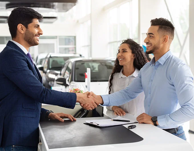 man and woman shaking hands with dealership salesman