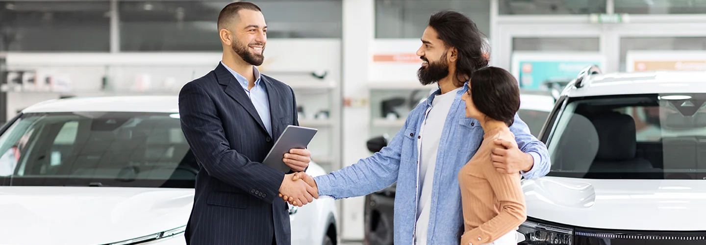 couple with a car salesperson in showroom shaking hands