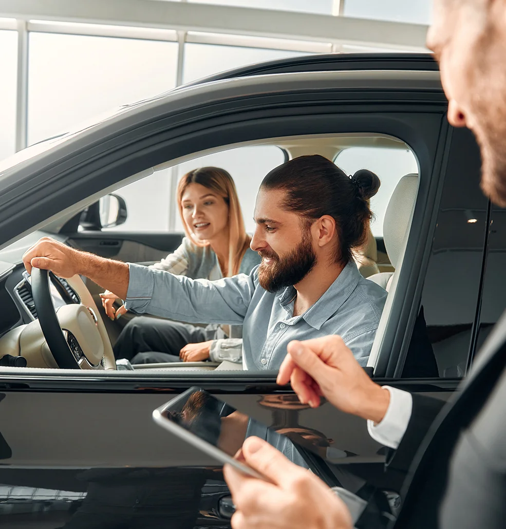 Inside a car, a man and woman are engaged with a tablet, appearing to discuss or review its content together.
