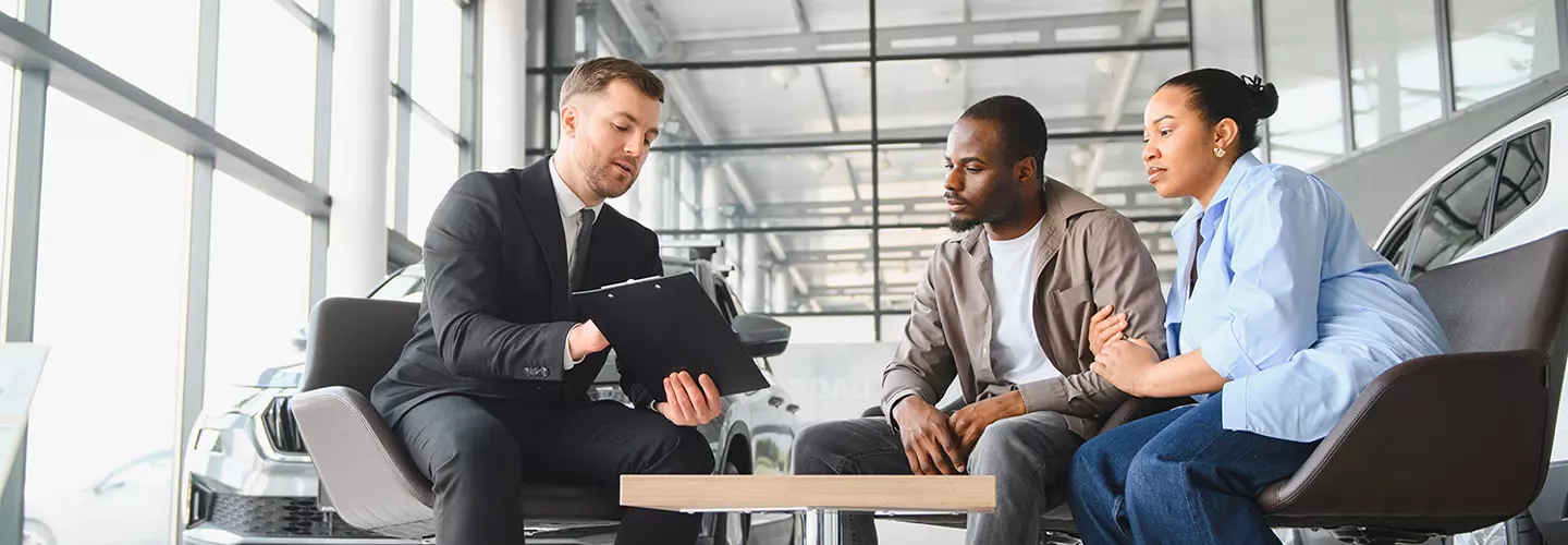 a couple sitting with car salesman going over details of a new car finance plan