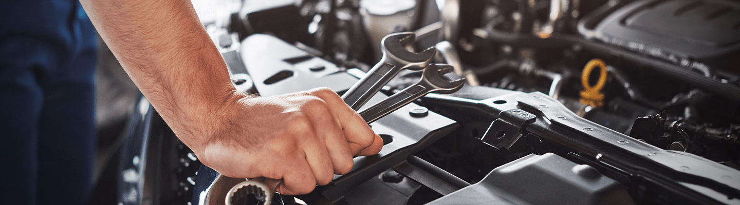 Close up view of a technician holding wrenches over a car engine