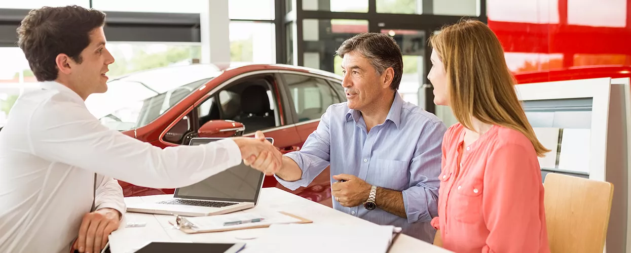 Car salesman talking to a couple and shaking hand