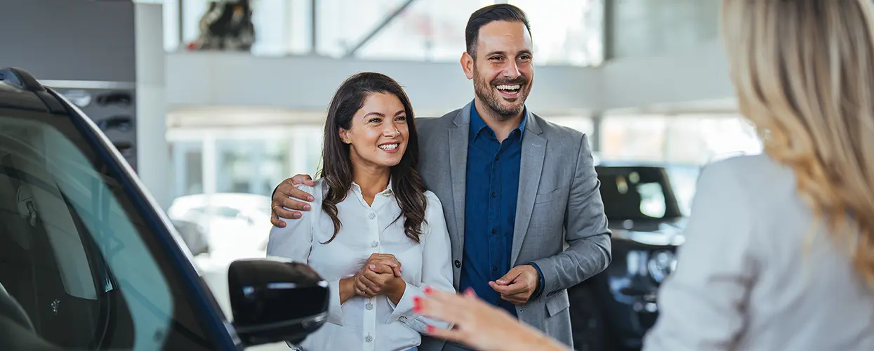 car salesperson showing ladies a new car to purchase in the deaership showroom