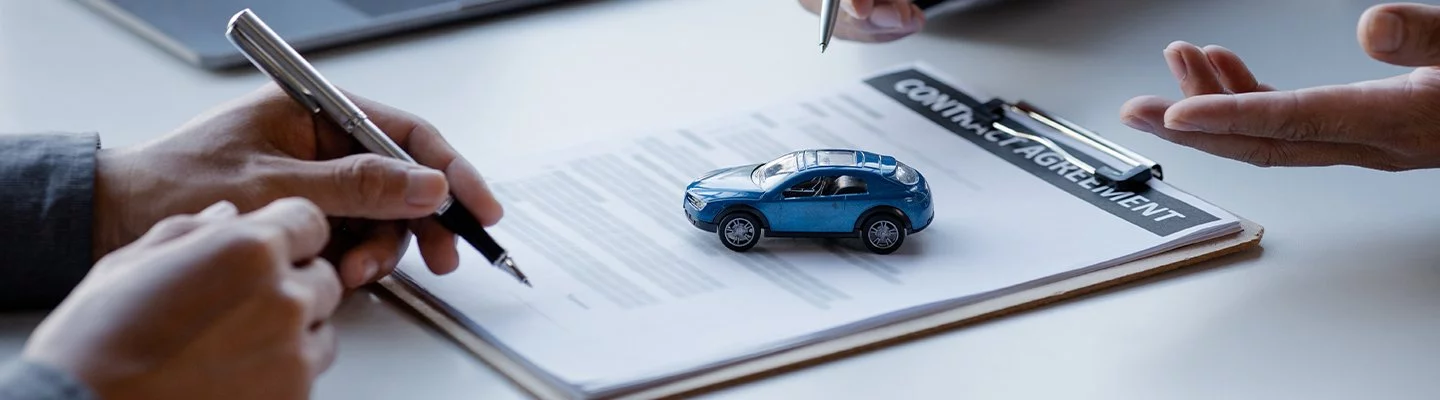 two people holding pens, looking over a contract agreement with a toy car on top