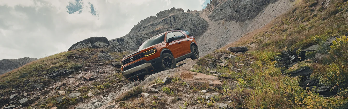 orange 2026 Honda Passport RTL offroad on a downhilll dirt slope in mountains