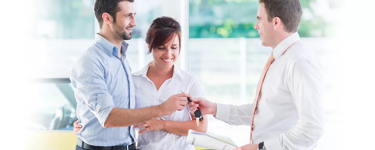 Car salesman handing keys to a couple