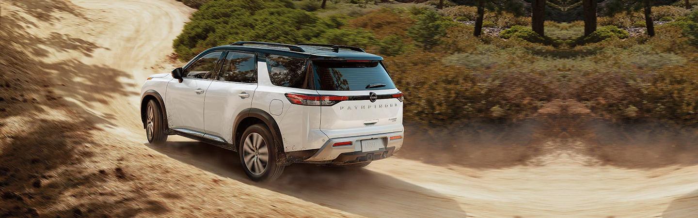 A white Nissan Pathfinder driving down a dirt road