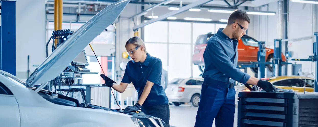 Two service mechanics working on a car with the hood up