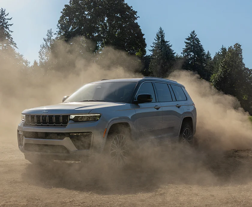 A 2026 Jeep Grand Cherokee navigating through a dusty landscape, highlighting its performance in challenging conditions.