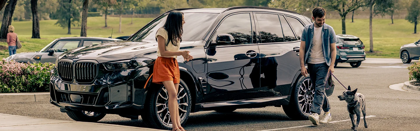 couple beside a BMW X5 sDrive40i please with their walking dog