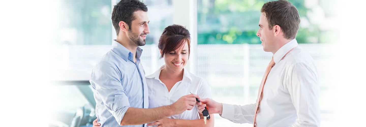 Sales person handing over keys to customers for there new car