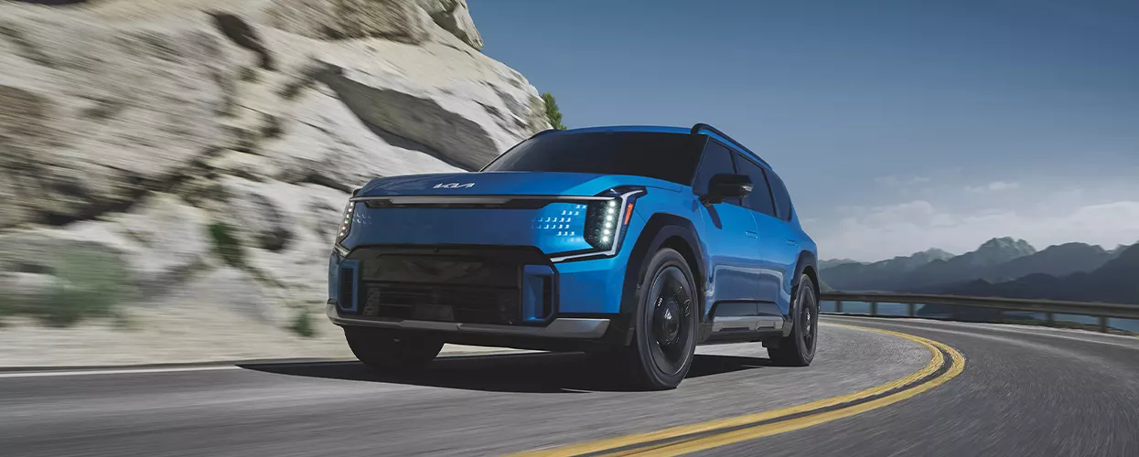 A blue Kia EV9 driving on a mountain side road