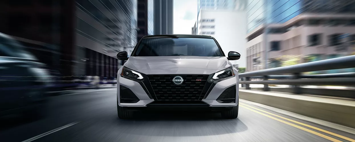 Front view of a white Nissan Altima driving fast though the city