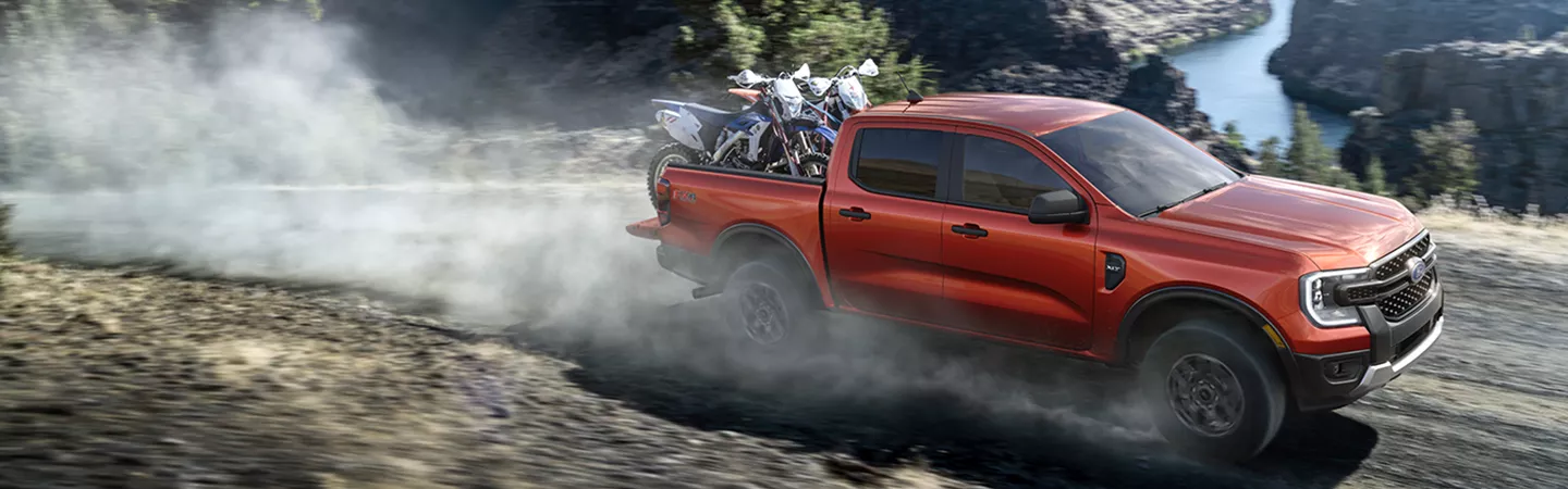 2025 Ford Ranger Raptor® driving on a dirt road with dirtbikes in the bed