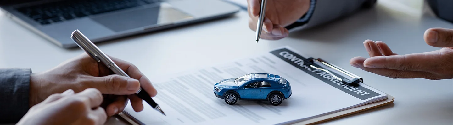 two people holding a pen and signing a contract with a model car on the papers