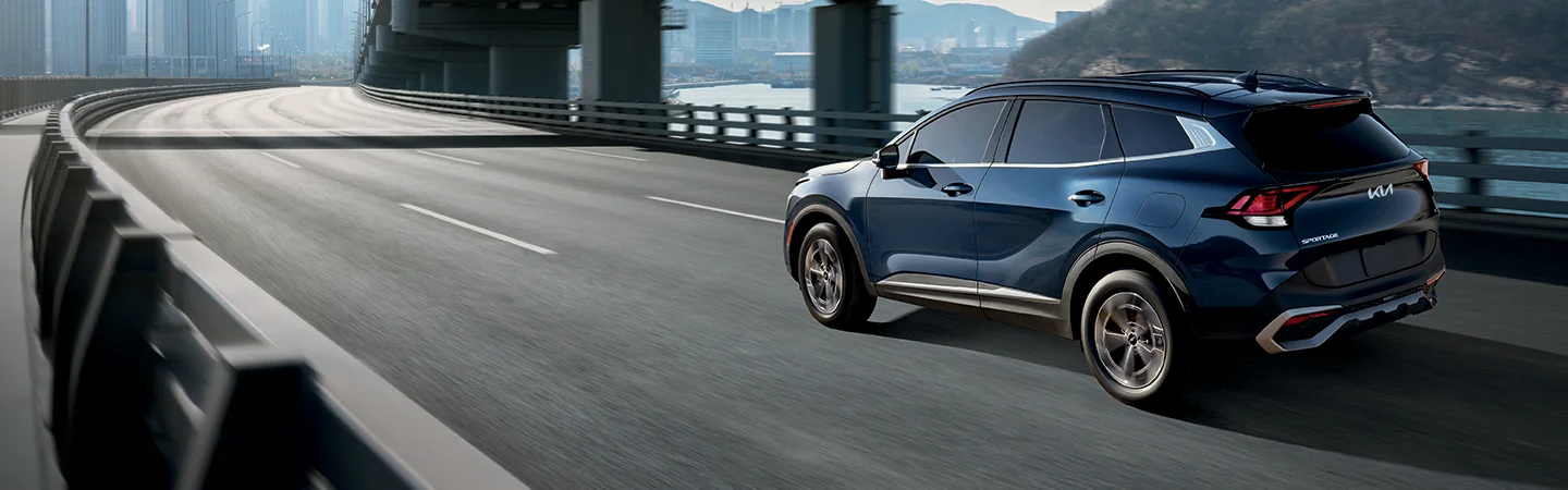 Side view of a blue 2025 Kia Sorento driving over a bridge in the city