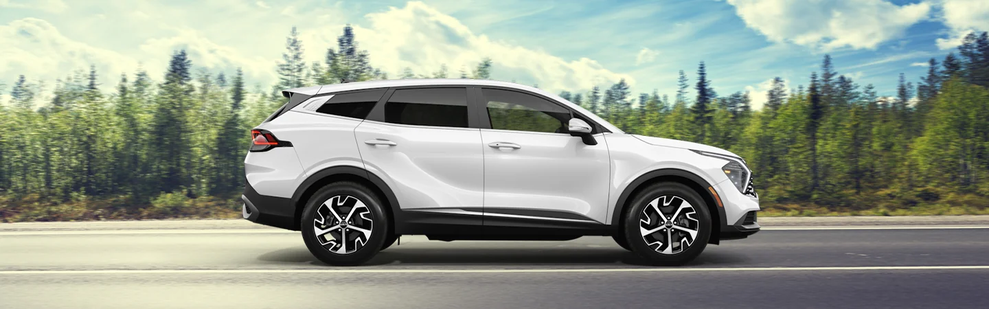 Side view of a white 2025 Kia Sportage with woods in the background
