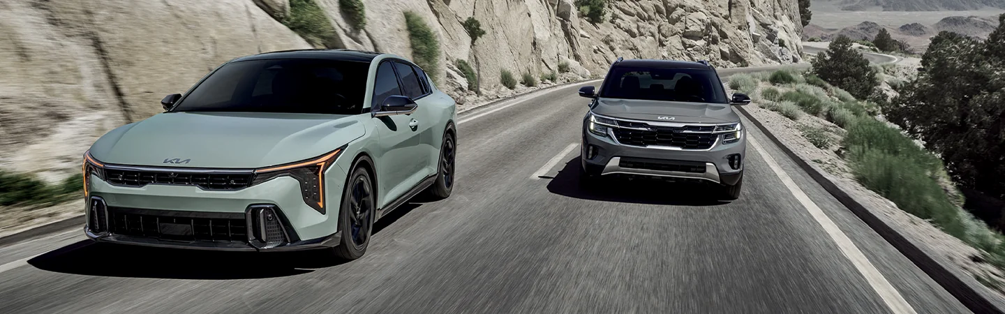 Side by side 2025 Kia K4 and a 2025 Kia K5 driving on a mountain side road