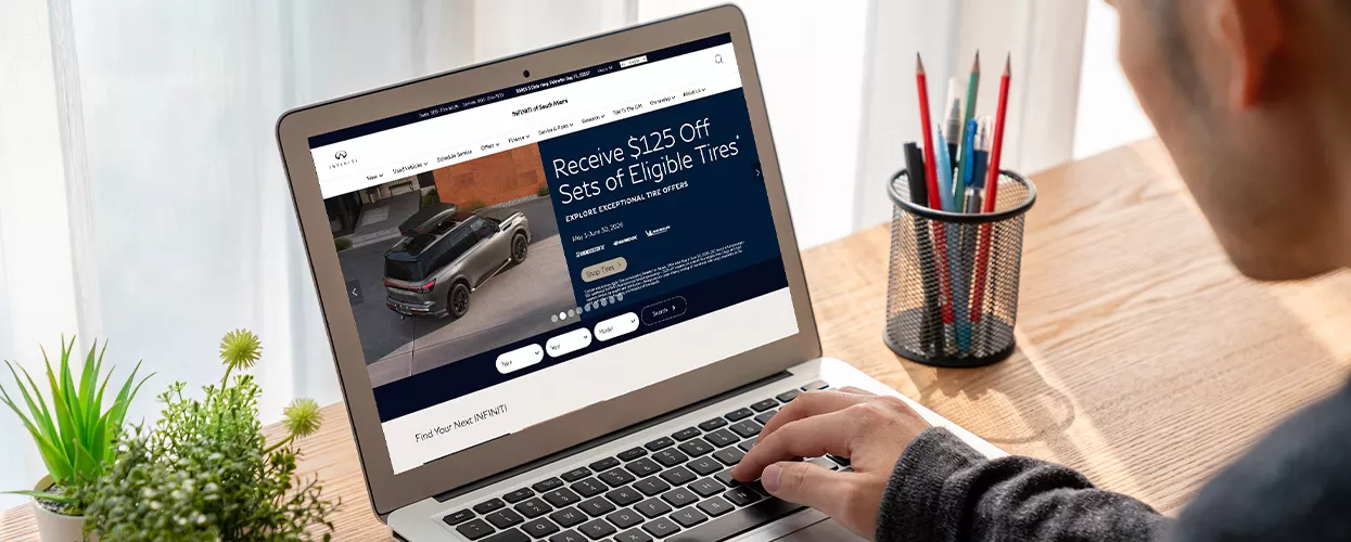 Customer exploring INFINITI vehicle specials and service offers on a dealership website using a laptop computer