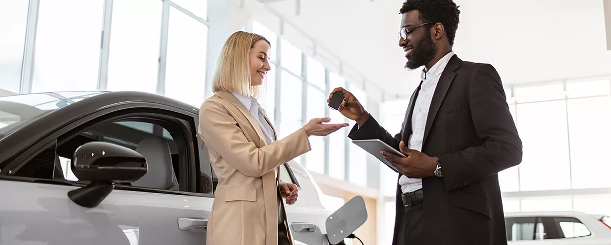 Sales person handing over car keys to a women that just bought a new car