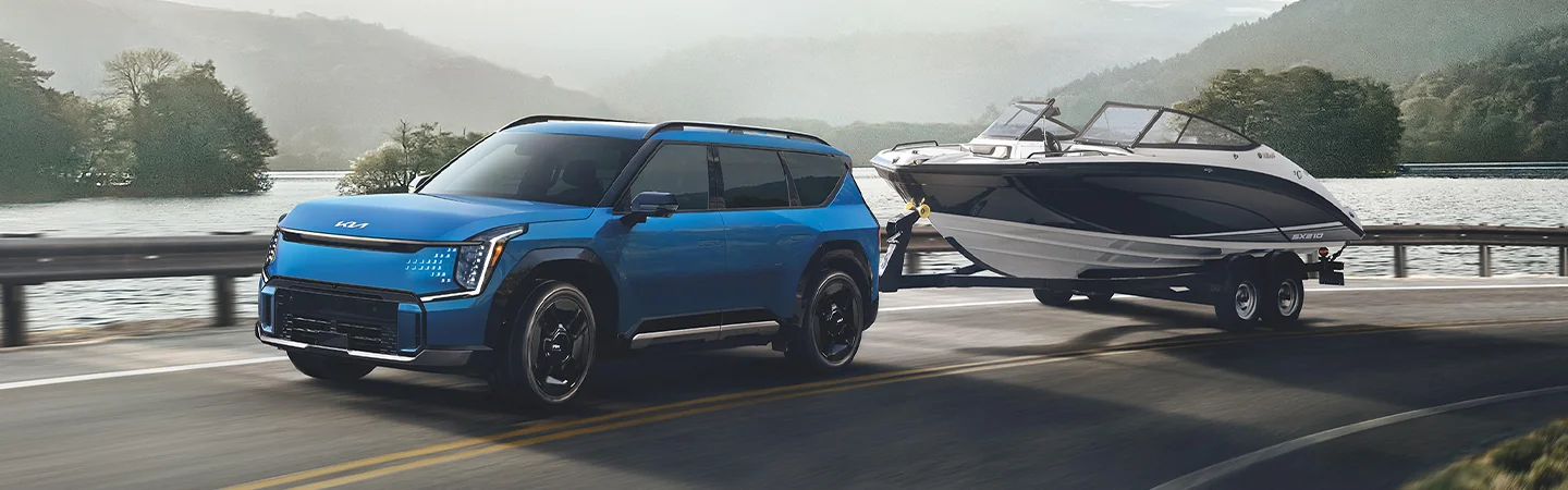 a blue 2026 Kia EV9 Light pulling a boat on trailer