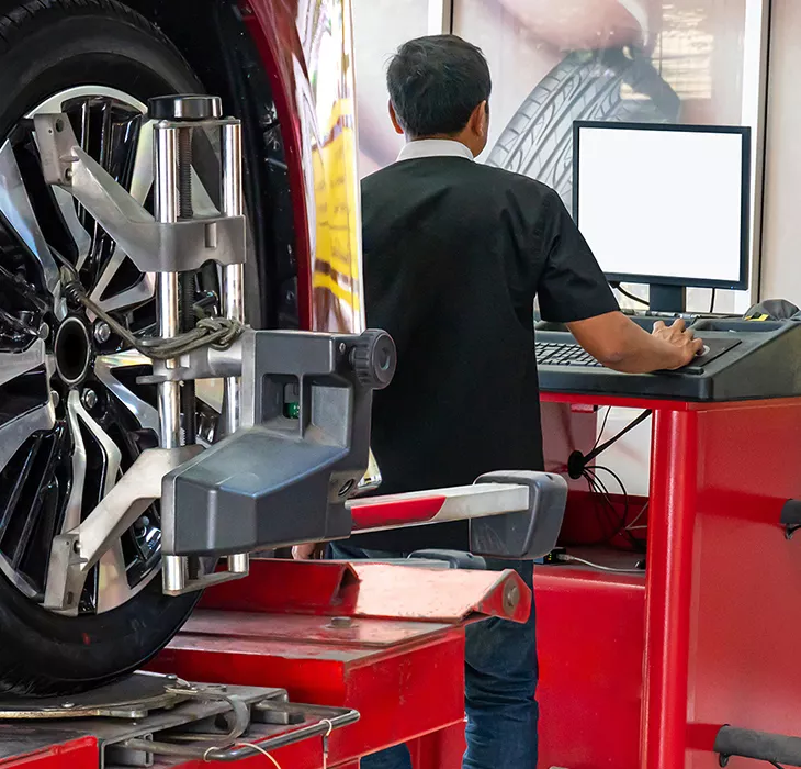 Automotive technician performing wheel alignment service using computerized alignment equipment in a professional auto repair shop