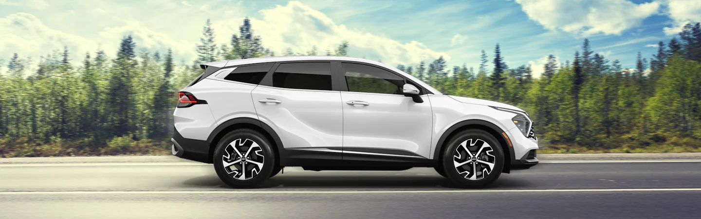 Side view of a white 2025 Kia Sportage Hybrid with a forest in the background