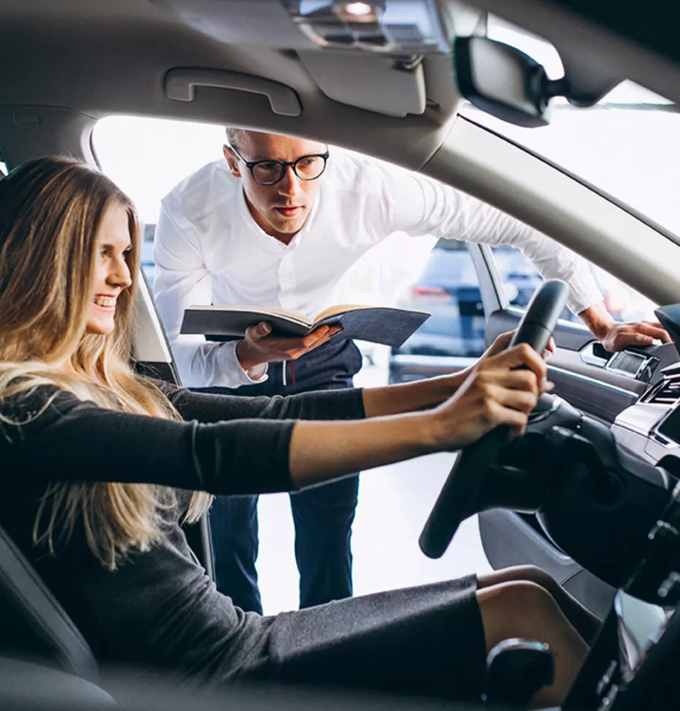 Woman sitting in a new vehiclw with a car salesman standing outside