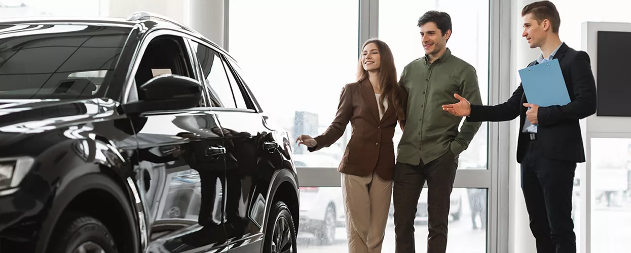 Couple looking at a new vehicle at a dealership with a car salmesman talking to them