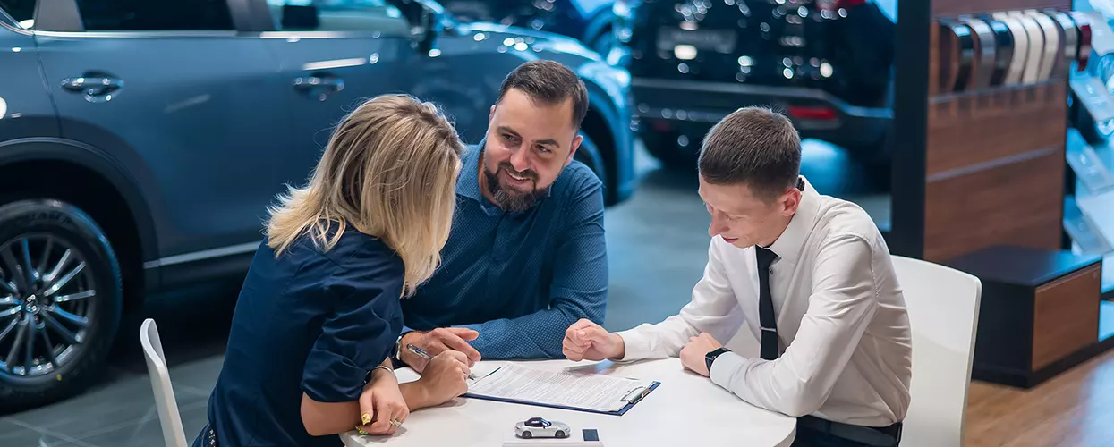 Couple speaking with car salesperson going over details of purchase at a table in showroom
