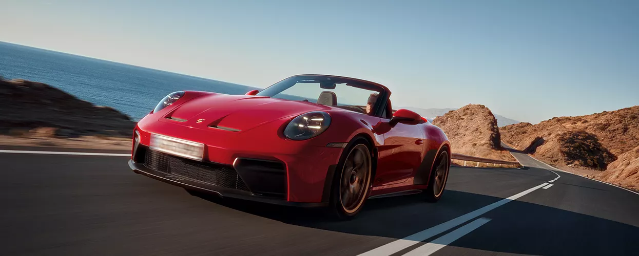 a red Porsche 911 driving on a scenic coastal road