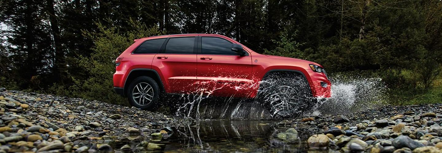 Red SUV driving over a small creek in the woods.