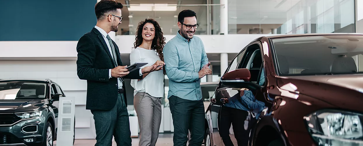 Which BMW Dealer is Best in Tampa? in Customers viewing a new sedan with a dealership sales consultant inside a modern automotive showroom