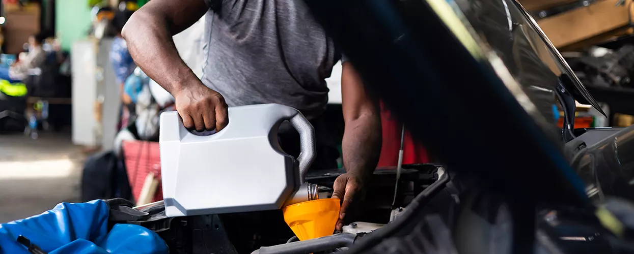 How Much Does an Oil Change Cost at Honda of Gainesville? in Auto service technician performing an oil change by adding engine oil during vehicle maintenance