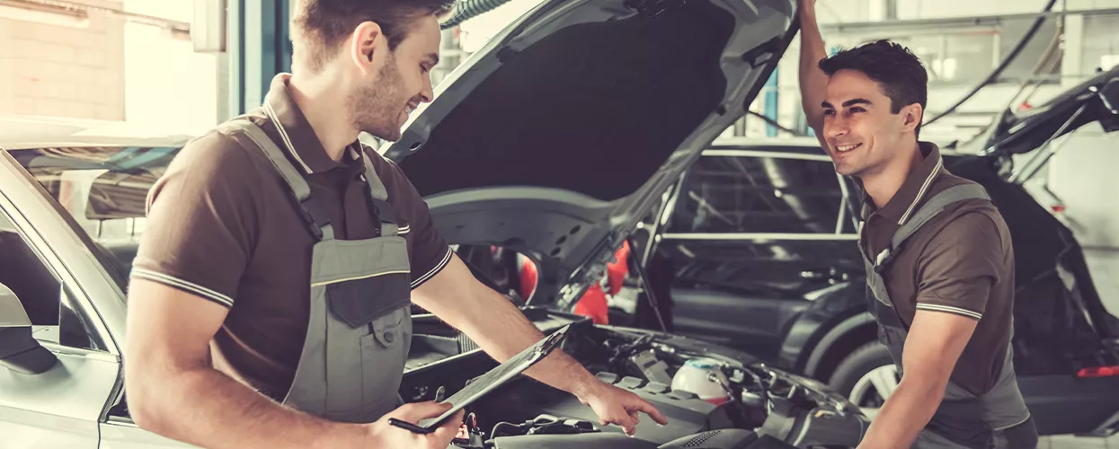 Two service mechanics working under the hood of a vehicle