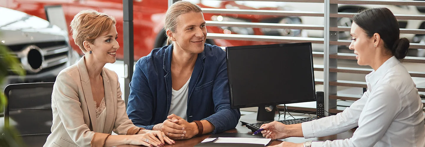 couple sitting at desk discussing car purchase with salesperson in car showroom