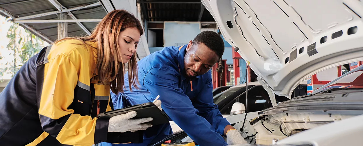 two people going over car repair in service bay looking inside engine at a dealership