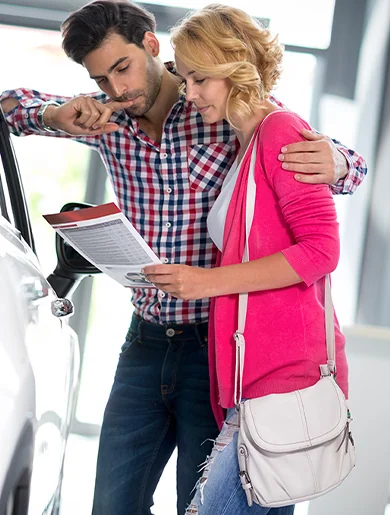 A couple inspects a car in a modern showroom, surrounded by other vehicles and promotional displays.