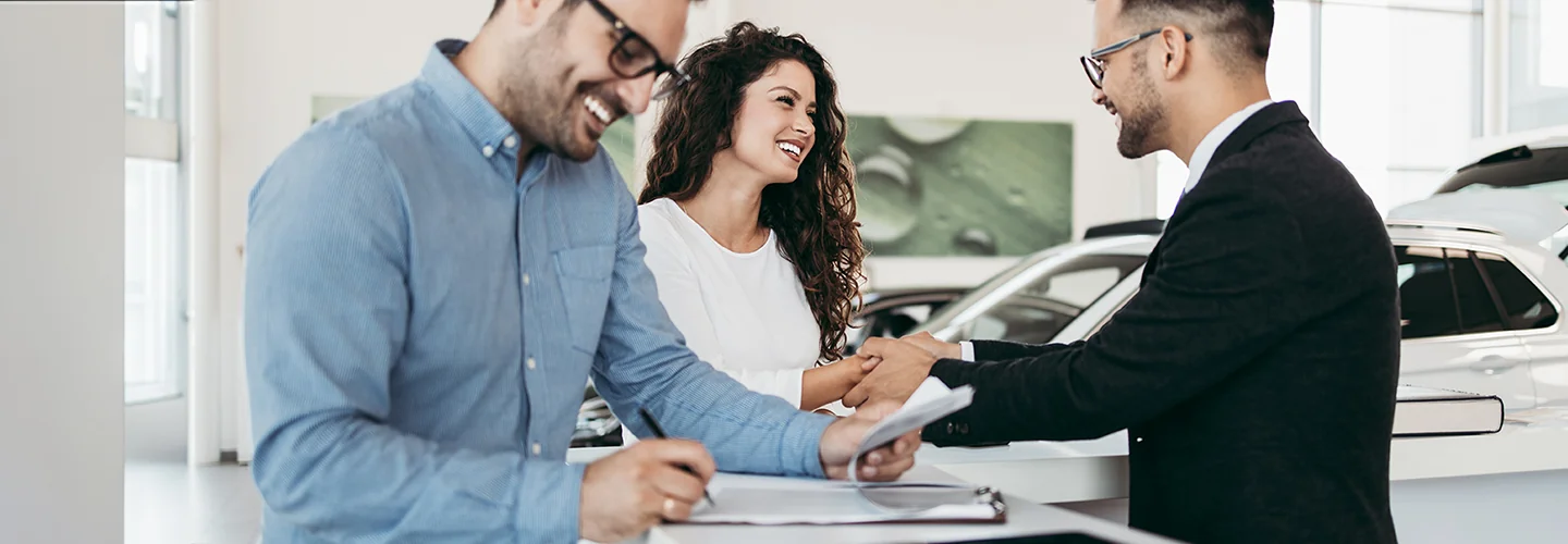 Man signing paperwork for new car and woman talking to car salesman