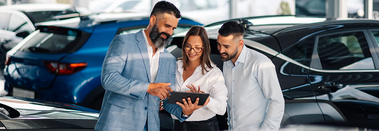 couple speaking with salesperson in car dealership showroom