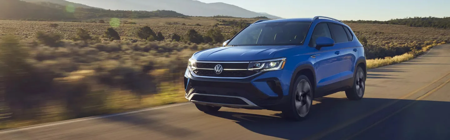 Front side view of a blue 2024 Volkswagen Taos driving on a road