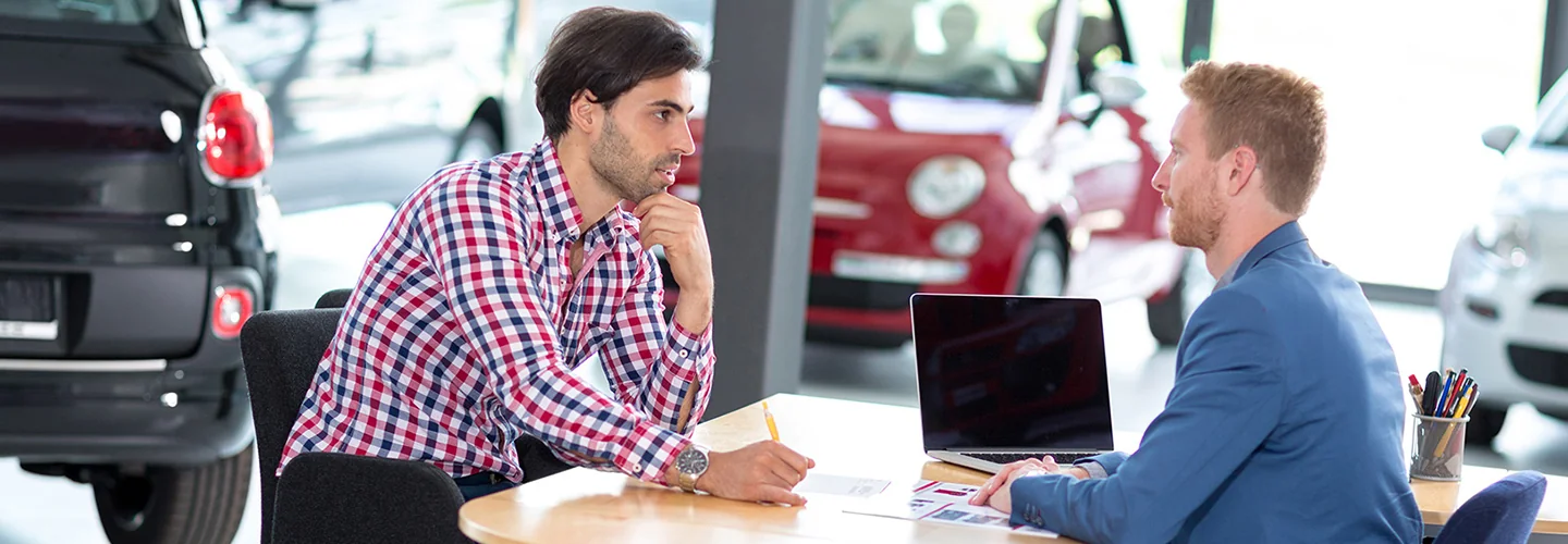 two people sitting in showroom at desk discussing car purchase