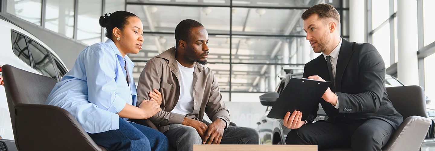 Two individuals sitting in a car dealership, discussing options together.