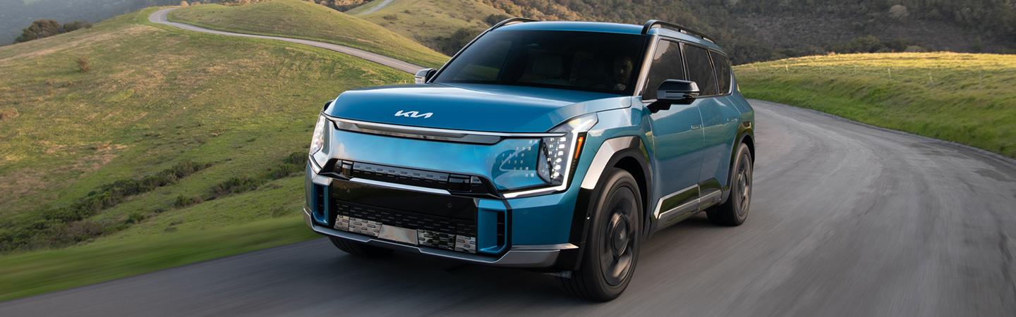 Front view of a teal 2024 Kia EV9 driving on the road