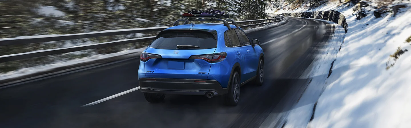 Back view of a blue 2026 Honda HR-V driving down a snowy road