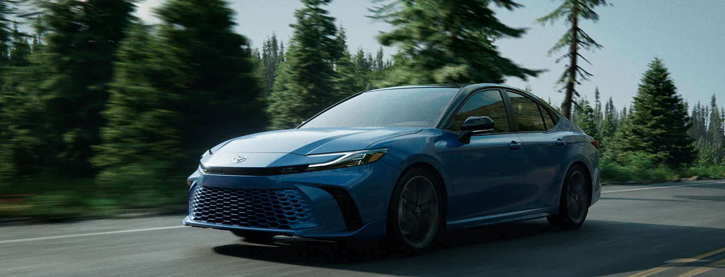 Toyota Camry driving down a mountain road with trees