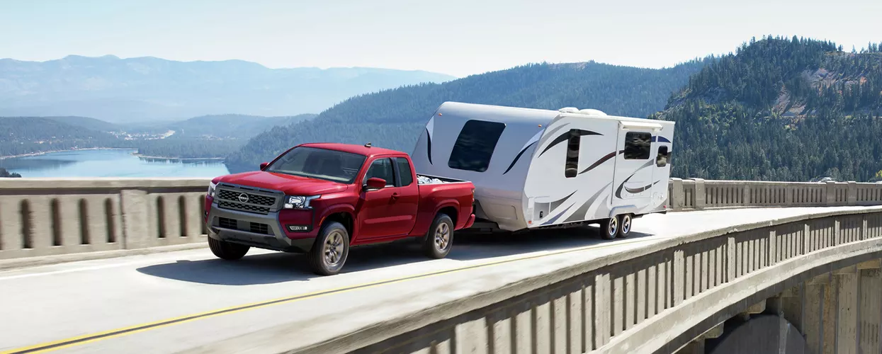 a Nissan Frontier towing a camper over a dam bridge with mountains in distance